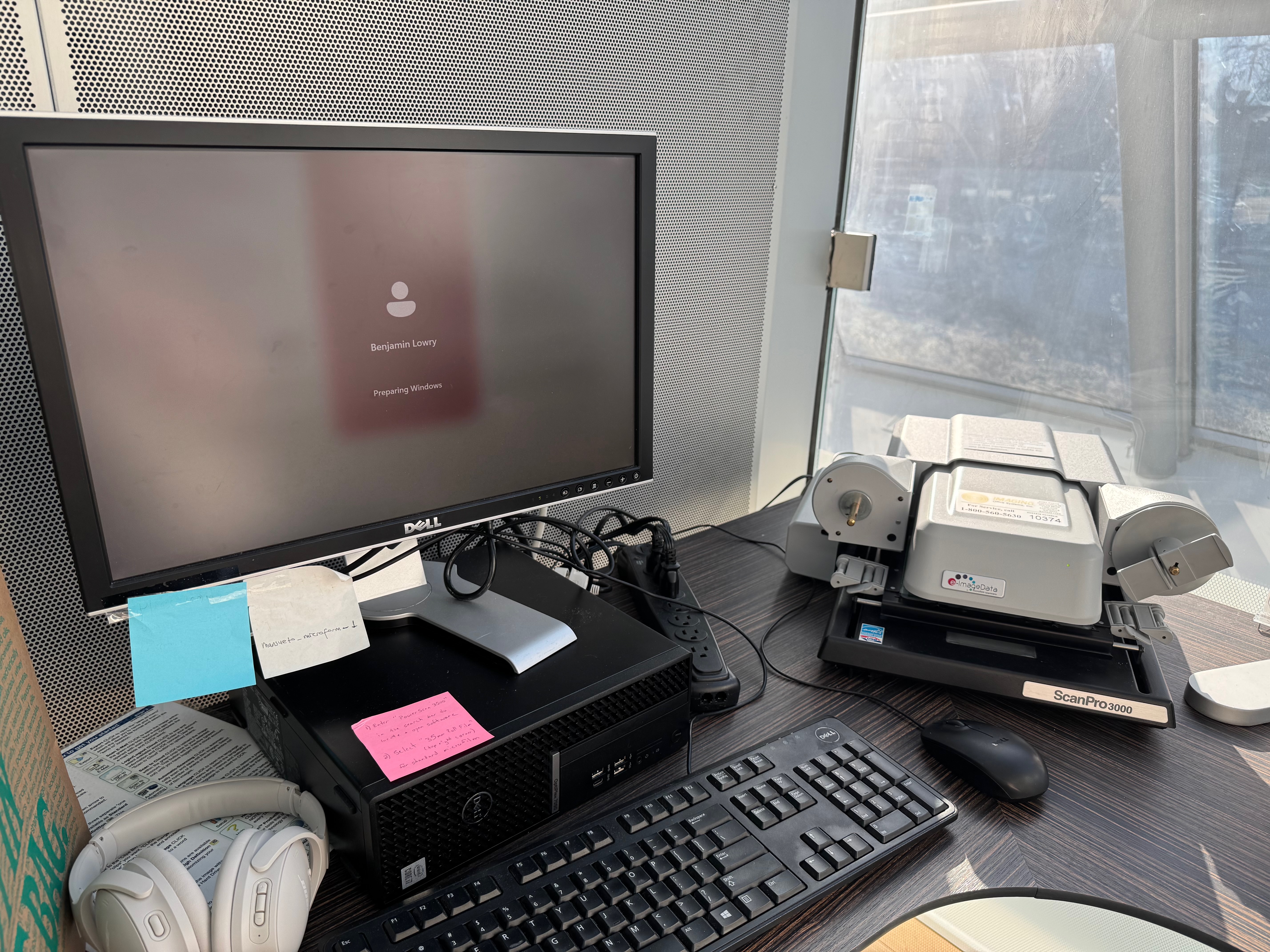 a Dell computer on a desk with keyboard, mouse, and a ScanPro 3000 microfiche scanner. The screen shows that the user Benjamin Lowry is logging into Windows